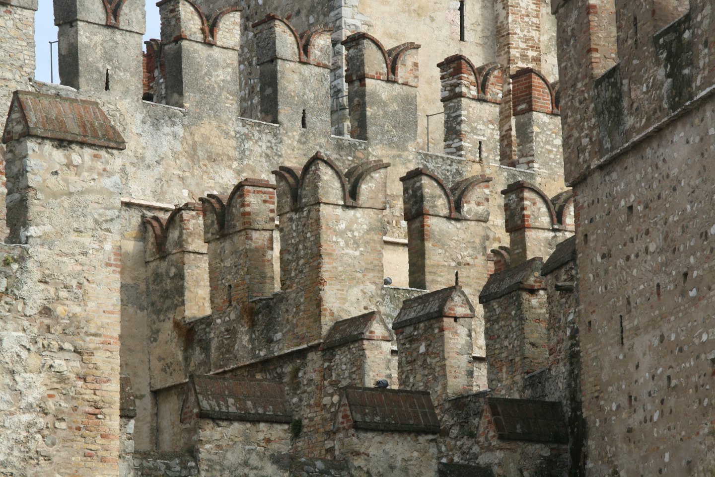 Verwitterte Stein- und rote Ziegelzinnen einer alten Burgmauer.