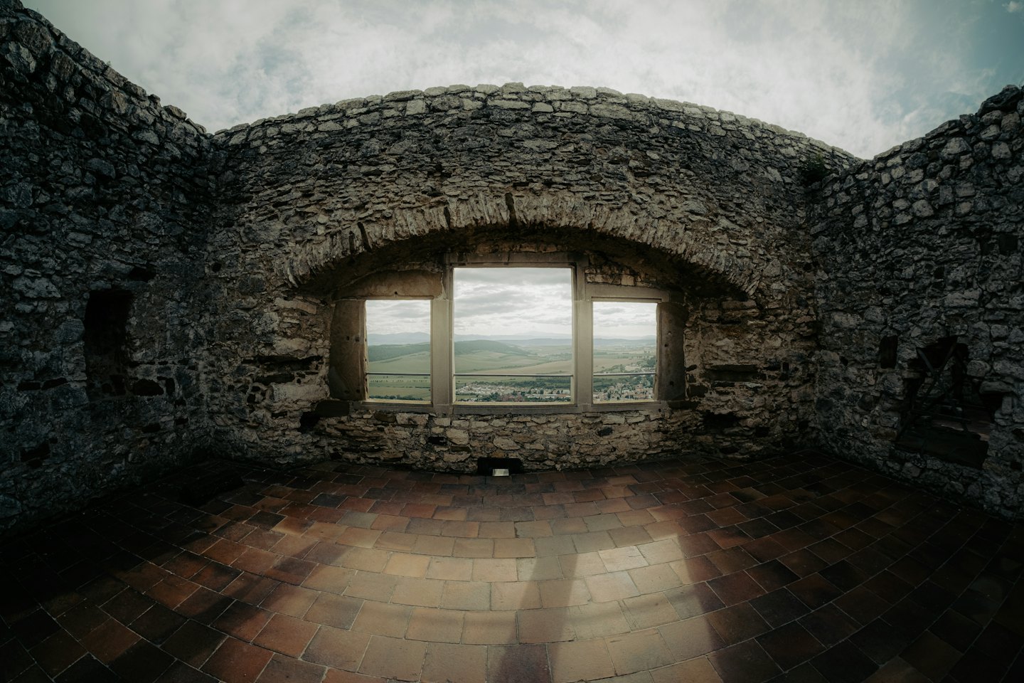 Steinerne Burgruine mit Bogenfenster und Blick auf grüne Hügel.
